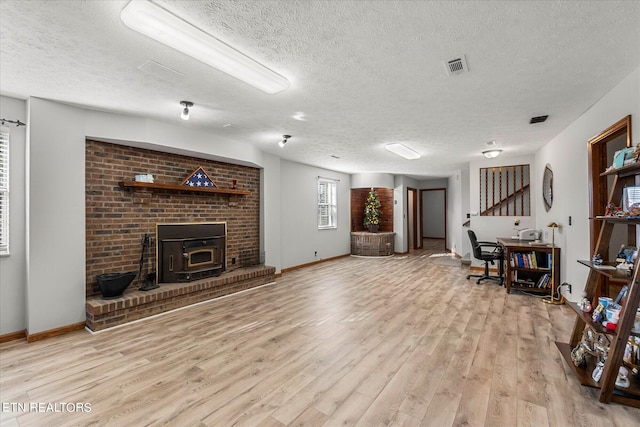 living room featuring a brick fireplace, a wood stove, light hardwood / wood-style floors, and a textured ceiling