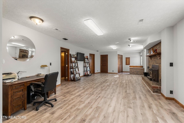 office with a textured ceiling, light wood-type flooring, and a fireplace