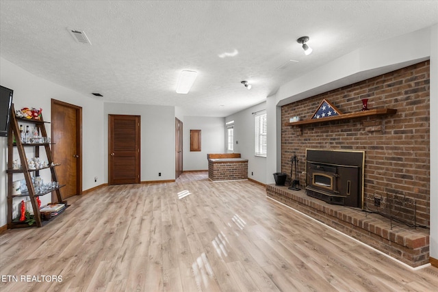 unfurnished living room featuring a wood stove, light hardwood / wood-style floors, and a textured ceiling