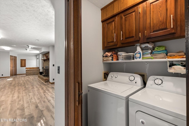 laundry room featuring a brick fireplace, light wood-type flooring, cabinets, washer and clothes dryer, and a textured ceiling