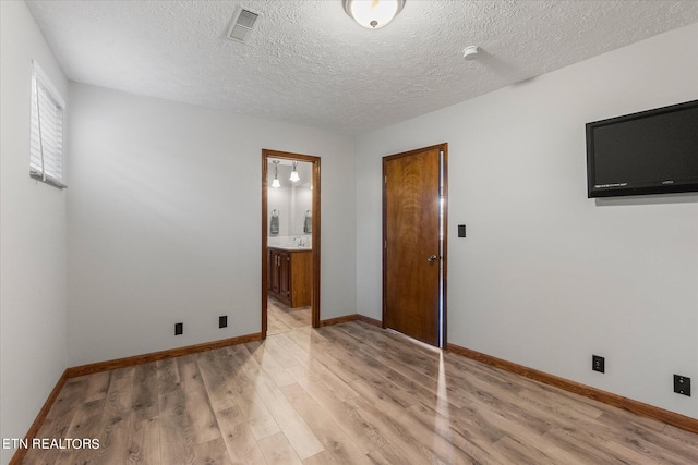 unfurnished bedroom featuring ensuite bath, a textured ceiling, and light hardwood / wood-style flooring