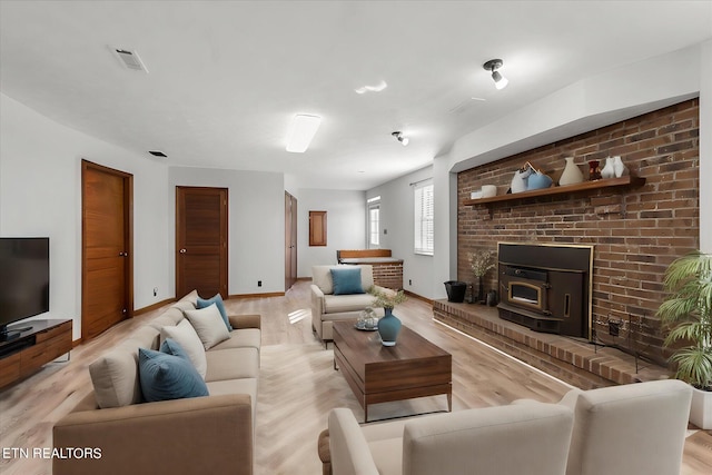 living room with a wood stove, light wood-type flooring, and a brick fireplace