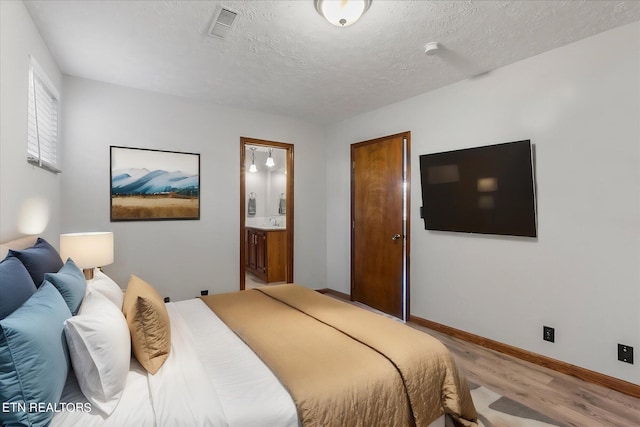 bedroom with a textured ceiling, light hardwood / wood-style flooring, and connected bathroom