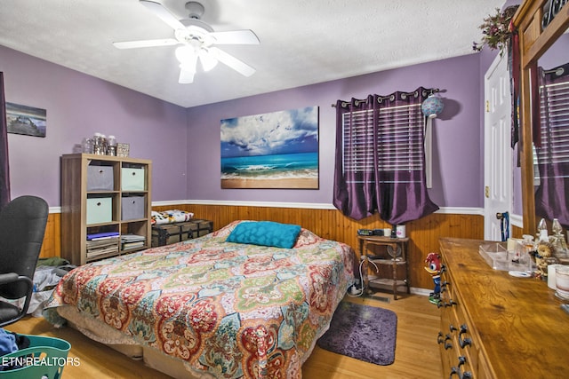 bedroom featuring a textured ceiling, wooden walls, ceiling fan, and light hardwood / wood-style floors