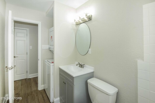 bathroom with vanity, toilet, hardwood / wood-style floors, and stacked washer / dryer