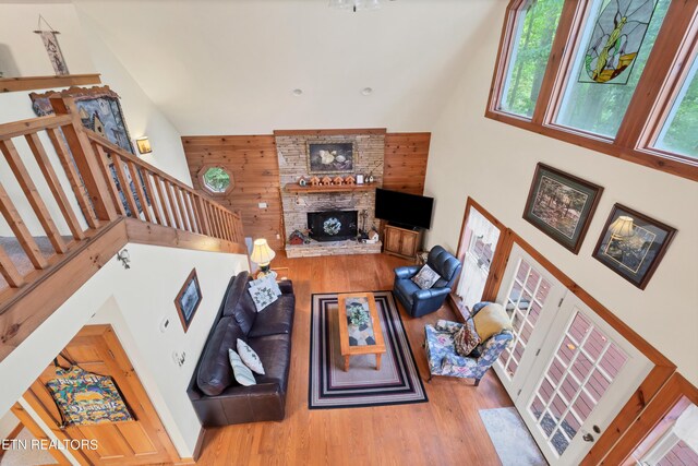 living room with a high ceiling, wood walls, wood-type flooring, and a fireplace