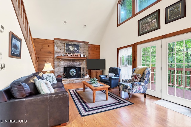 living room featuring hardwood / wood-style floors, a stone fireplace, high vaulted ceiling, and wooden walls