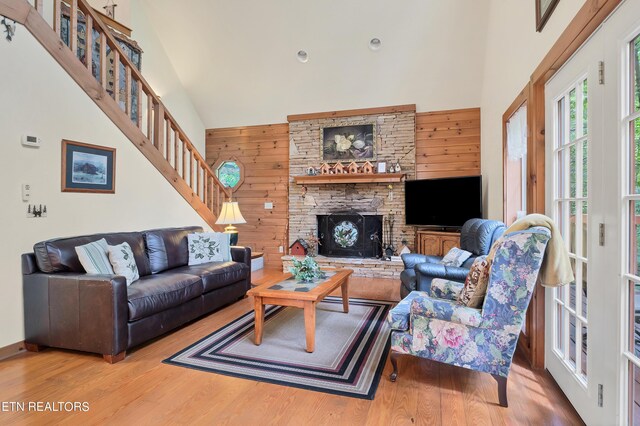 living room with high vaulted ceiling, wood walls, wood-type flooring, and a fireplace