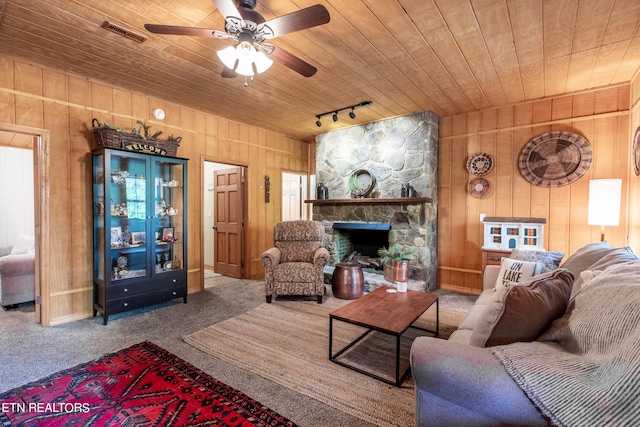 living room featuring ceiling fan, wood ceiling, a stone fireplace, carpet, and rail lighting