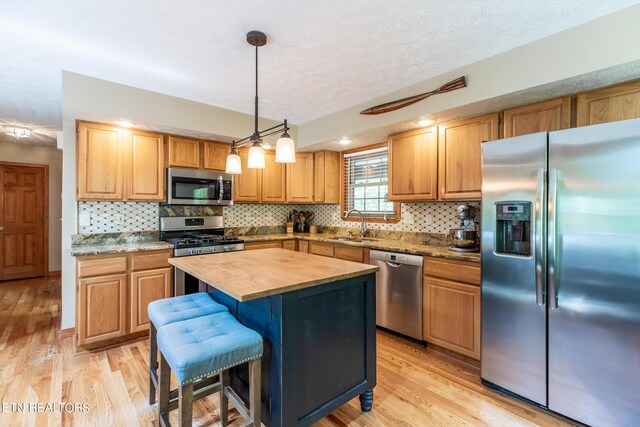 kitchen featuring pendant lighting, a kitchen island, light hardwood / wood-style flooring, appliances with stainless steel finishes, and wood counters