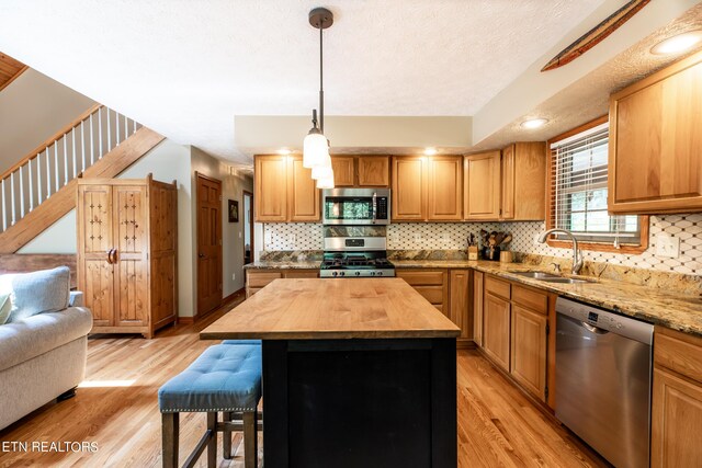 kitchen with light hardwood / wood-style floors, a center island, sink, appliances with stainless steel finishes, and wooden counters