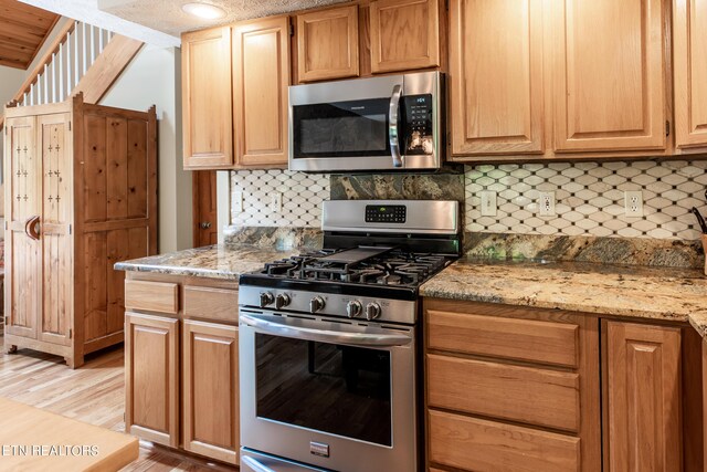 kitchen featuring light stone countertops, appliances with stainless steel finishes, tasteful backsplash, and light hardwood / wood-style flooring