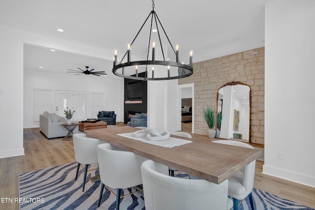 dining space with ceiling fan with notable chandelier, light wood-type flooring, and a fireplace