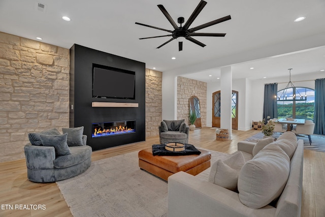 living room featuring ceiling fan with notable chandelier, light hardwood / wood-style floors, and a fireplace