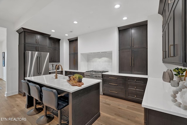 kitchen featuring a breakfast bar area, a center island with sink, light hardwood / wood-style floors, and appliances with stainless steel finishes