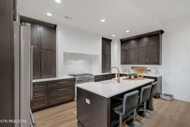 kitchen featuring stainless steel appliances, a kitchen breakfast bar, light hardwood / wood-style flooring, backsplash, and a kitchen island with sink