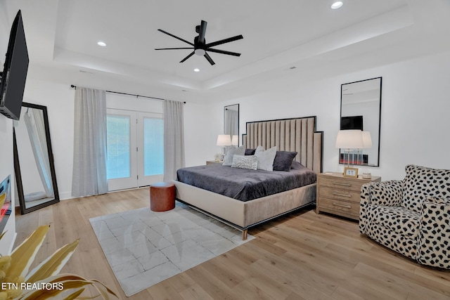 bedroom with access to exterior, light wood-type flooring, a tray ceiling, and ceiling fan