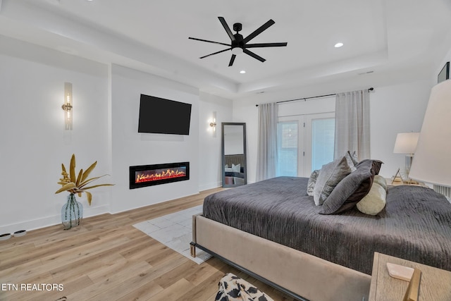 bedroom featuring ceiling fan, a raised ceiling, light wood-type flooring, and access to outside