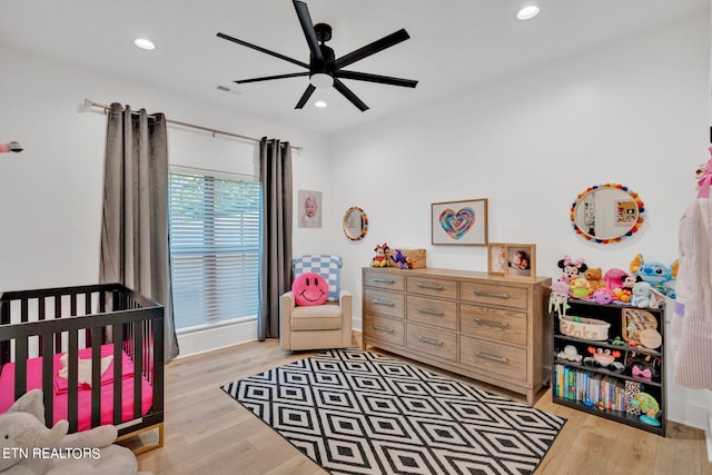 bedroom featuring light wood-type flooring, a nursery area, and ceiling fan