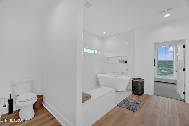 bathroom with hardwood / wood-style flooring, a healthy amount of sunlight, toilet, and a bath