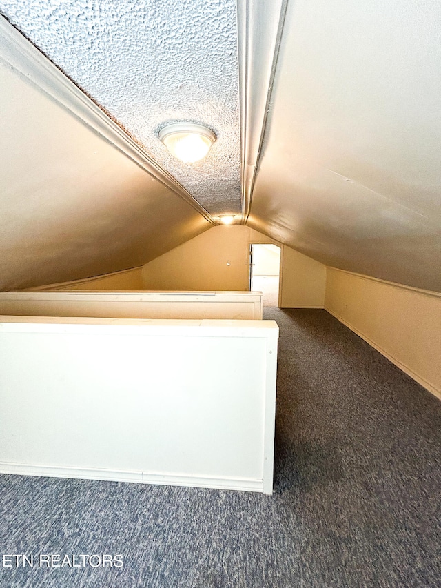 bonus room featuring lofted ceiling, a textured ceiling, and dark carpet