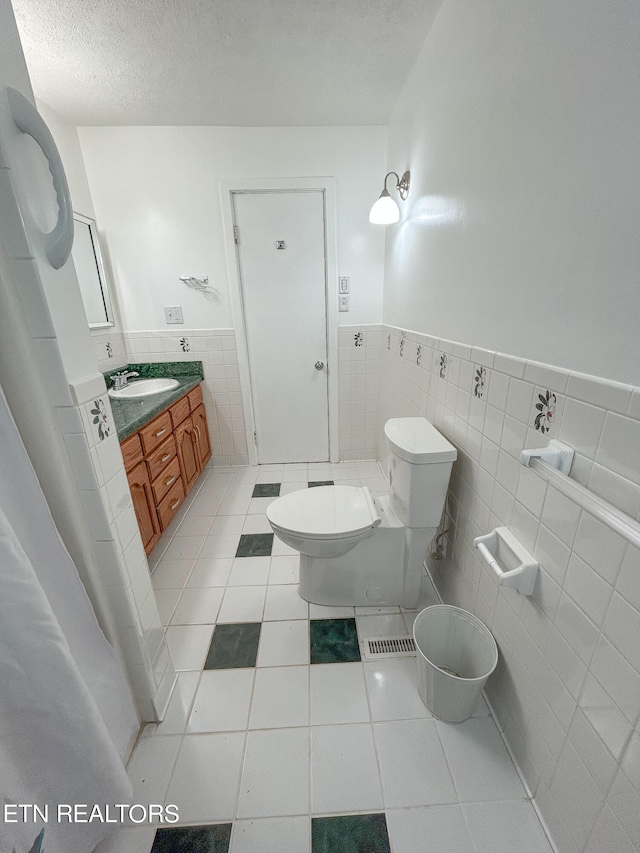 bathroom featuring a textured ceiling, tile walls, toilet, vanity, and tile patterned flooring