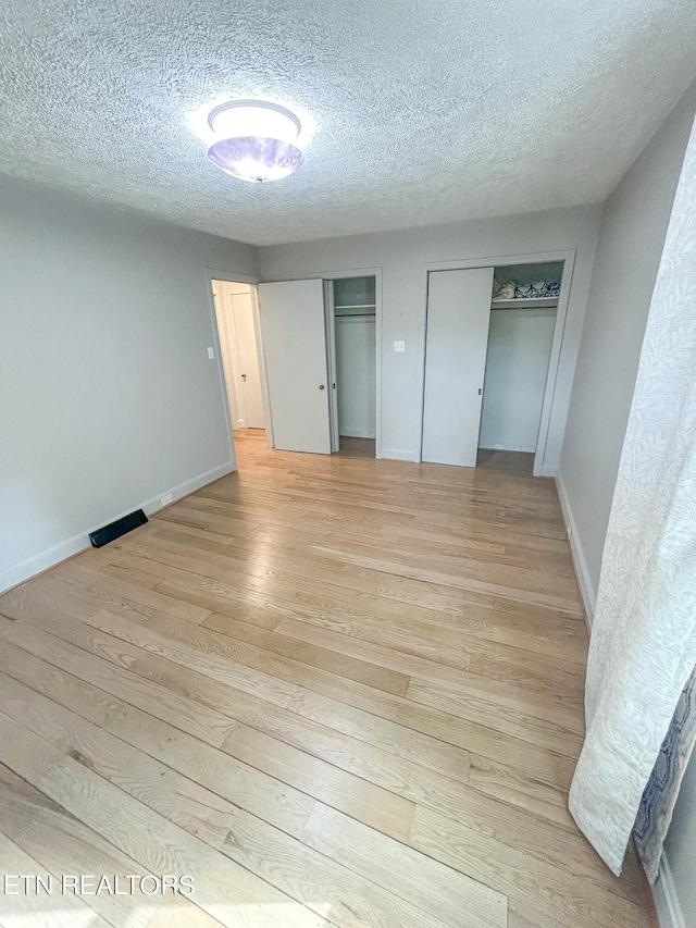 unfurnished bedroom featuring light hardwood / wood-style floors, a textured ceiling, and two closets