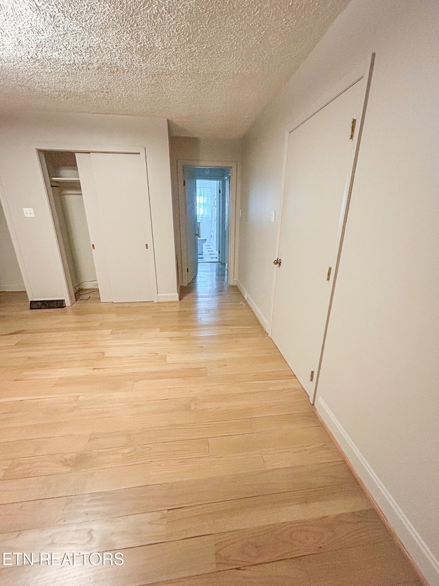 hallway with light hardwood / wood-style flooring and a textured ceiling