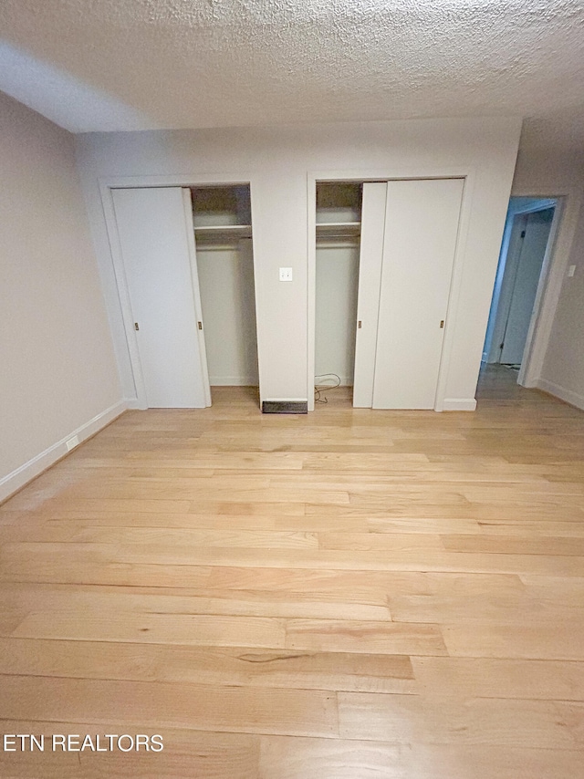 unfurnished bedroom with a textured ceiling, light wood-type flooring, and two closets