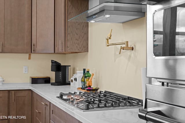 kitchen with stainless steel gas stovetop, light stone counters, and extractor fan