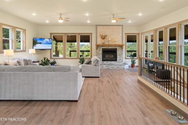 living room featuring a wealth of natural light, light hardwood / wood-style floors, ceiling fan, and a stone fireplace