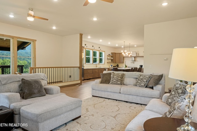 living room with ceiling fan with notable chandelier, light wood-type flooring, and sink