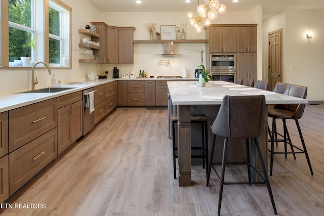 kitchen with light wood-type flooring, sink, a kitchen bar, hanging light fixtures, and appliances with stainless steel finishes