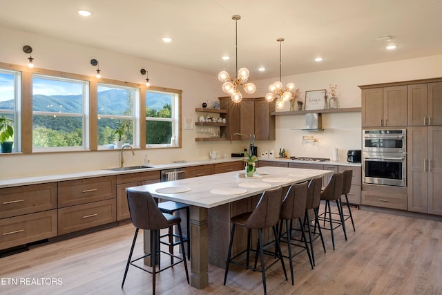 kitchen with light wood-type flooring, a center island, sink, and wall chimney range hood