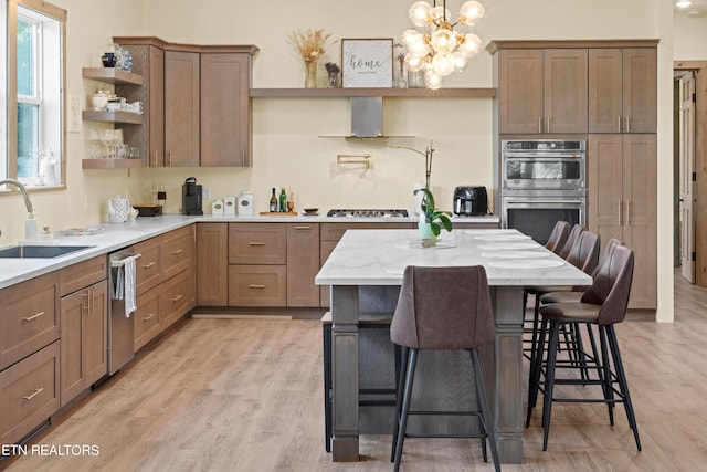 kitchen featuring a breakfast bar, stainless steel appliances, light wood-type flooring, sink, and wall chimney range hood