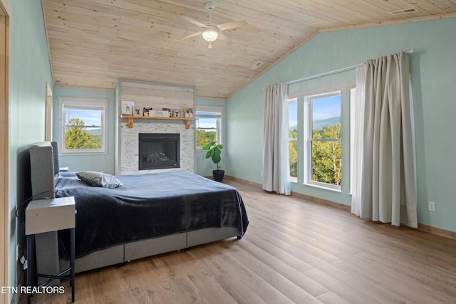 bedroom with vaulted ceiling, a stone fireplace, wooden ceiling, light wood-type flooring, and ceiling fan