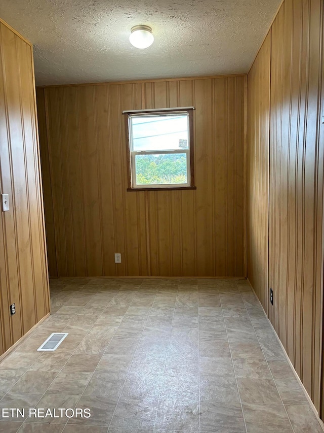 unfurnished room featuring wooden walls and a textured ceiling