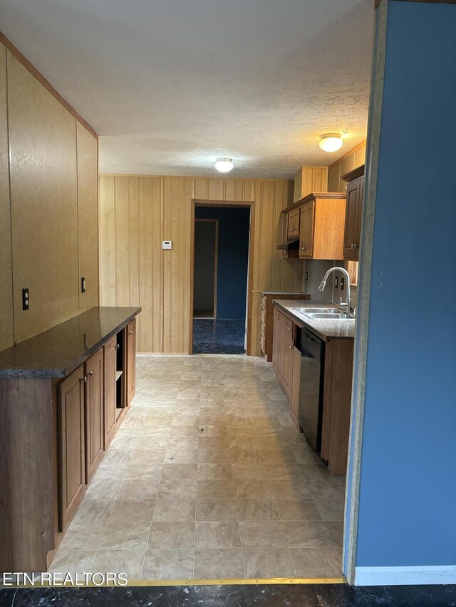 kitchen with black dishwasher, a textured ceiling, sink, and wooden walls