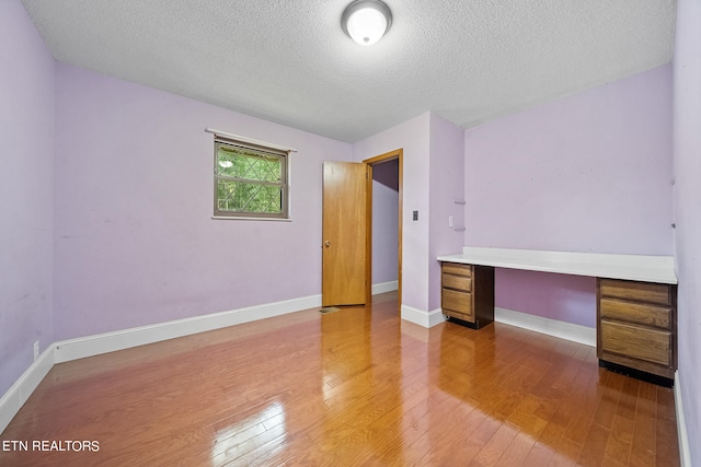 interior space with a textured ceiling, built in desk, and hardwood / wood-style flooring