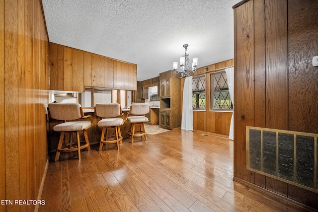 interior space featuring light wood-type flooring, wood walls, a notable chandelier, and a textured ceiling