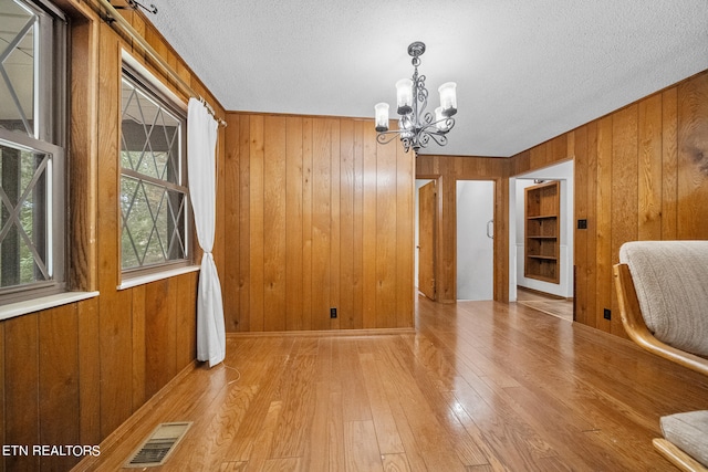 unfurnished dining area with a textured ceiling, a notable chandelier, light wood-type flooring, and wooden walls