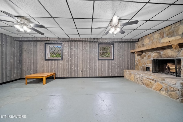 basement with ceiling fan, a stone fireplace, and a drop ceiling