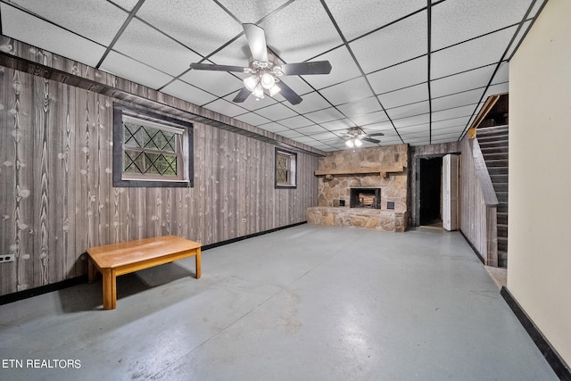 basement with a paneled ceiling, ceiling fan, wood walls, and a fireplace