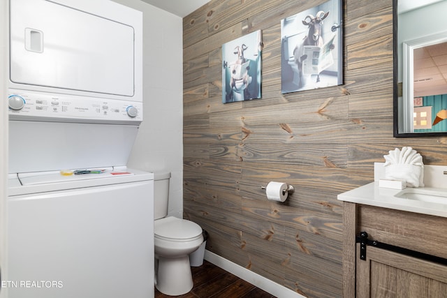 bathroom with vanity, stacked washer / dryer, hardwood / wood-style flooring, wooden walls, and toilet