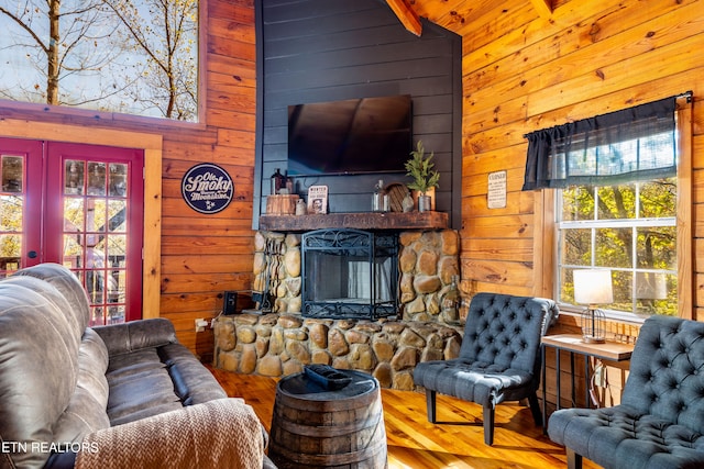 living room with wood walls, a stone fireplace, vaulted ceiling, and hardwood / wood-style flooring