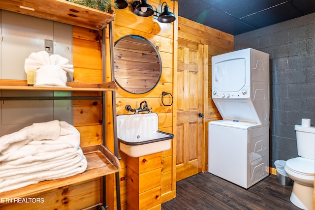 bathroom with wooden walls, stacked washer and dryer, toilet, and hardwood / wood-style flooring