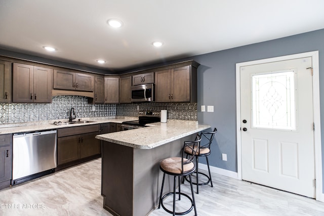 kitchen with dark brown cabinets, a kitchen bar, stainless steel appliances, sink, and light stone countertops