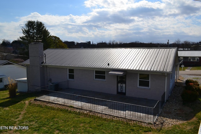 back of property with a standing seam roof, a yard, a chimney, brick siding, and metal roof