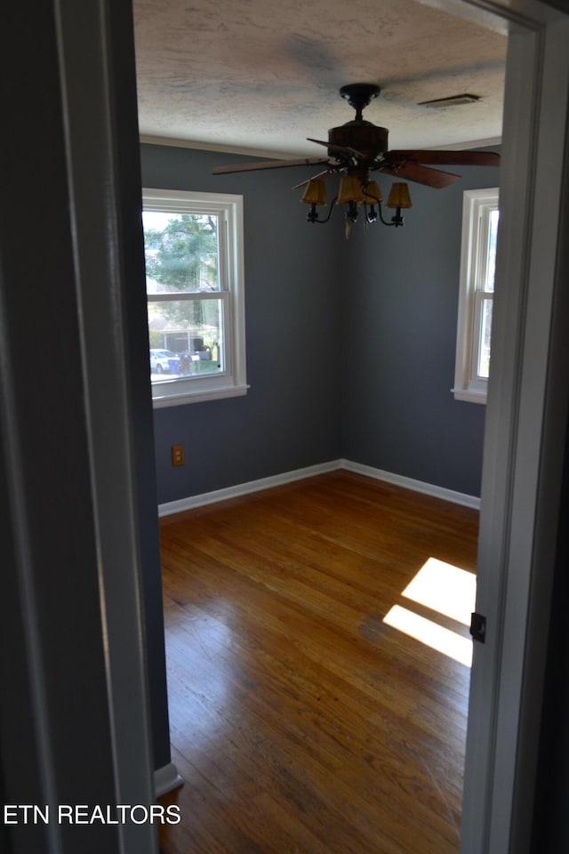 spare room featuring ceiling fan, wood finished floors, baseboards, and a textured ceiling