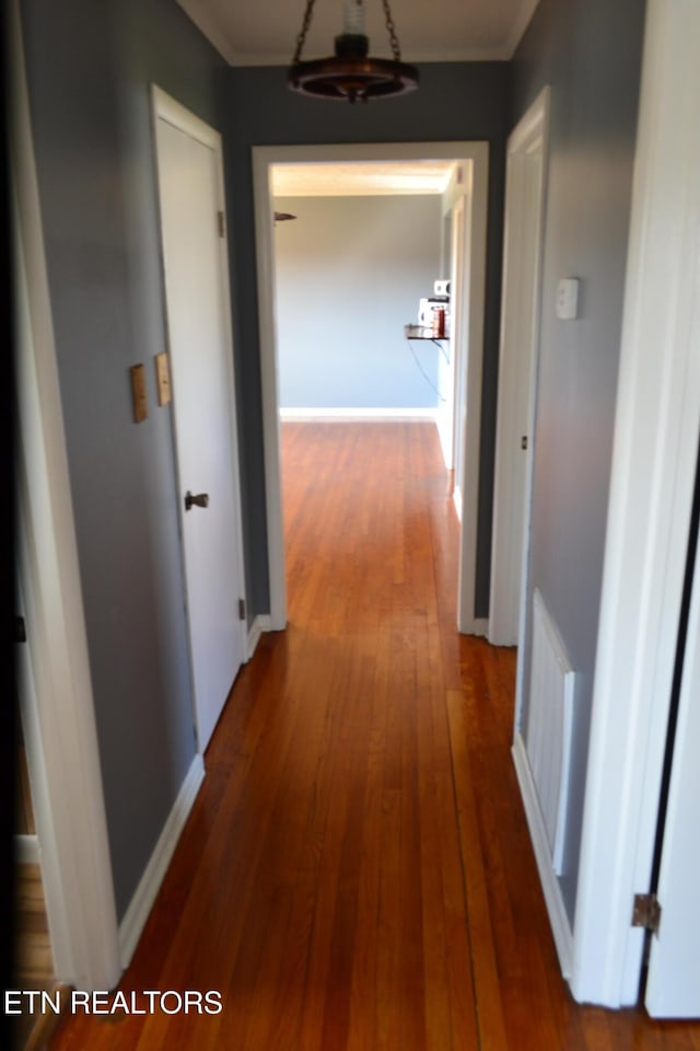 hall featuring hardwood / wood-style floors, baseboards, and ornamental molding